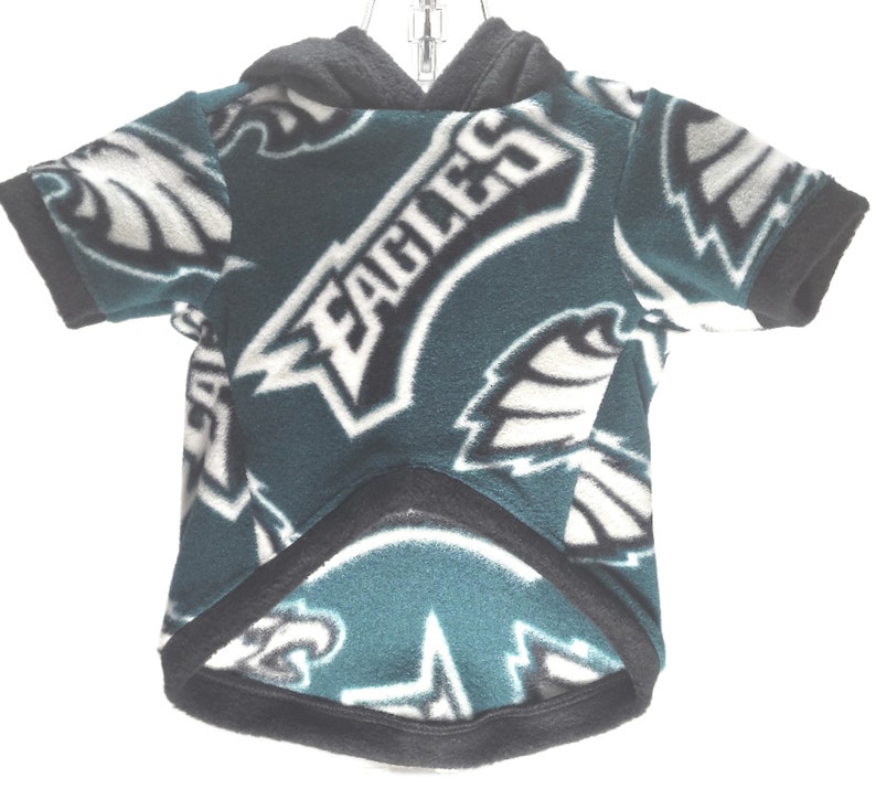 May include: Green, black, and white fleece dog hoodie with the Philadelphia Eagles logo repeated all over. The hoodie has a hood with a black drawstring.