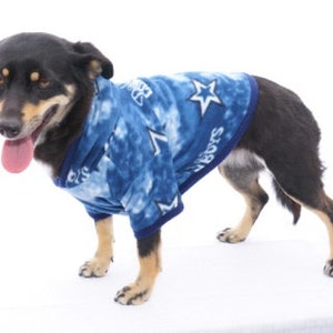 May include: A black and brown dog wearing a blue and white fleece dog sweater with a star pattern and the word "Stars" on it.