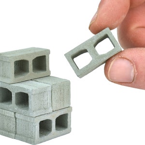 May include: A stack of four miniature concrete blocks, each with two rectangular holes, on a white background. A single block is held in a hand.