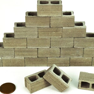 K&ouml;nnte beinhalten: Ein Stapel grauer Betonbl&ouml;cke, die in Pyramidenform angeordnet sind. An der Basis befinden sich vier Bl&ouml;cke, in der n&auml;chsten Reihe drei und so weiter. Die Bl&ouml;cke sind etwa 5 cm hoch und 10 cm breit. Im Vordergrund befindet sich ein Penny als Gr&ouml;&szlig;envergleich.