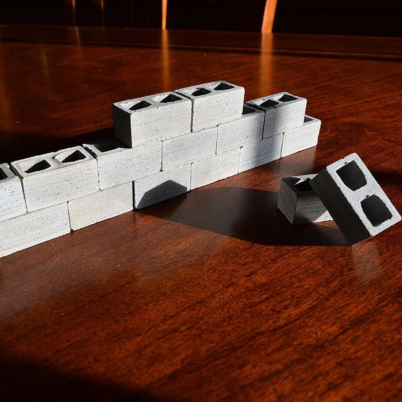 K&ouml;nnte beinhalten: Eine Miniatur-Mauer aus grauen Betonbl&ouml;cken. Die Mauer ist teilweise gebaut und es liegen ein paar zus&auml;tzliche Bl&ouml;cke auf der Holzoberfl&auml;che.