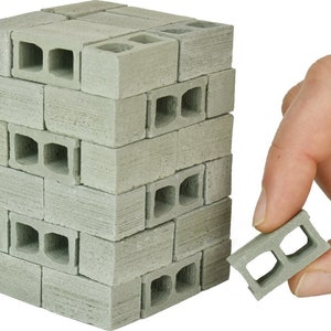 K&ouml;nnte beinhalten: Ein Stapel Miniatur-Betonsteine, jeder mit zwei L&ouml;chern, in hellgrauer Farbe. Ein einzelner Stein wird in der Hand gehalten, wodurch die Details der L&ouml;cher sichtbar werden.