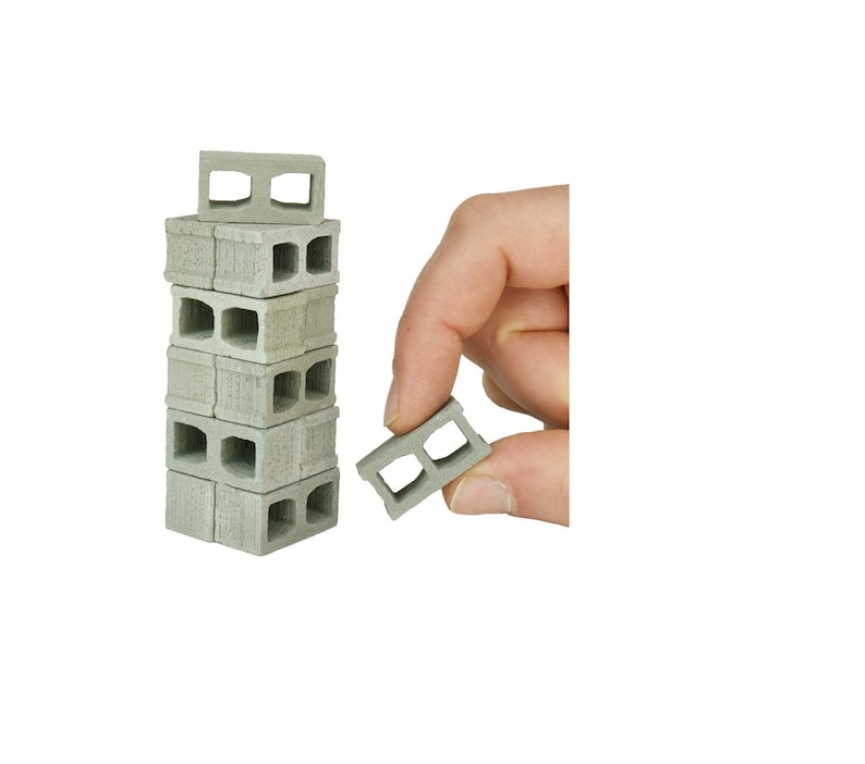 K&ouml;nnte beinhalten: Ein Stapel Miniatur-Betonsteine, wobei ein Stein in einer Hand gehalten wird. Die Steine sind grau und haben eine raue Textur.