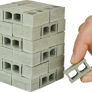 May include: A stack of miniature concrete blocks, each with two holes, in a light gray color. A single block is held in a hand, showing the detail of the holes.