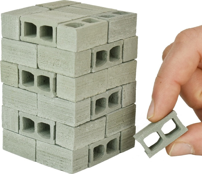 May include: A stack of miniature concrete blocks, each with two holes, in a light gray color. A single block is held in a hand, showing the detail of the holes.