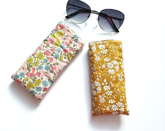 May include: Two rectangular fabric pouches and a pair of black sunglasses. One pouch features a multi-coloured floral pattern with yellow, pink, and blue flowers on a white background. The other pouch has a mustard yellow background with white flowers.