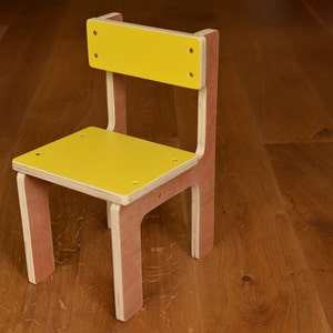 May include: A small wooden chair with a yellow seat and backrest. The chair has a natural wood frame with visible grain and is held together with small screws. The chair is designed for children.
