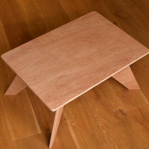 May include: A small, rectangular wooden table with a natural finish. The table has a simple design with angled legs, and is approximately 46 cm long and 30 cm wide. The table is made of light-coloured wood.
