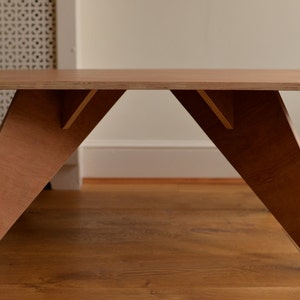 May include: A light brown wooden coffee table with a rectangular top and angled legs. The table has a minimalist design. The V-shaped legs provide stability. The table's dimensions are approximately 120 cm long, 60 cm wide, and 40 cm high.