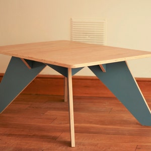 May include: A rectangular wooden coffee table with a light wood top and teal-coloured legs. The legs are angled, creating a modern design. The table is approximately 76 cm long and 51 cm wide.