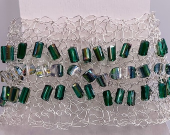 May include: A wide cuff bracelet constructed from silver-toned wire mesh, featuring a series of rectangular, faceted beads in shades of emerald green and iridescent clear glass woven throughout the intricate, open-work metallic structure.