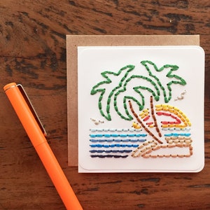 May include: A white card with a colorful embroidered design of palm trees, a beach, and a sunset. The embroidery is done with colorful thread and the card is perfect for a summer greeting.
