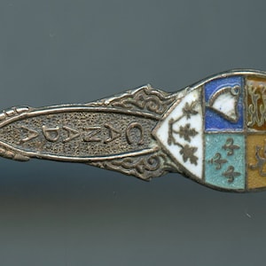 May include: Silver souvenir spoon with a blue, white, and gold enamel design on the handle. The bowl of the spoon is engraved with the word "Quebec".