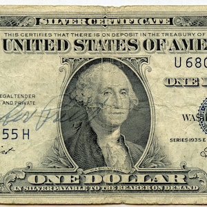 May include: A vintage one dollar silver certificate featuring a portrait of George Washington. The certificate is dated 1935 and has the serial number U68066755 H.