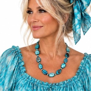 May include: A necklace featuring oval-shaped beads in shades of turquoise and teal with a marbled pattern, interspersed with small black spacer beads. The beads are arranged in a single strand, creating a continuous circular design around the neck.