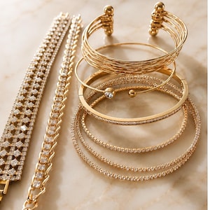 May include: A collection of gold-toned bracelets including a wide multi-row rhinestone cuff, a delicate chain bracelet with clear stones, a multi-strand wire cuff, a hinged bangle with a single stone, and two thin, flexible rhinestone tennis bracelets.