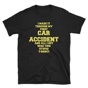 Può includere: T-shirt nera con testo giallo. Il testo recita: "I MADE IT THROUGH MY FIRST CAR ACCIDENT AND ALL I GOT WAS THIS STUPID T-SHIRT!". La maglietta ha un girocollo e maniche corte.