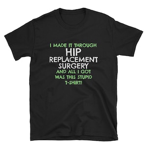 May include: Black t-shirt featuring the text "I MADE IT THROUGH HIP REPLACEMENT SURGERY AND ALL I GOT WAS THIS STUPID T-SHIRT!" in white and green. The shirt has a crew neck and short sleeves.