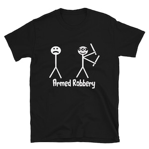 May include: Black t-shirt featuring a white graphic of two stick figures. One has a sad face, the other a mask and weapons. The words "Armed Robbery" are printed below the figures in white.
