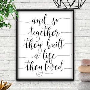 Könnte beinhalten: Schwarz-weiß Typografie-Druck mit dem Text "and so together they built a life they loved". Der Druck ist in einem schwarzen Rahmen gerahmt und hängt an einer weißen Backsteinwand.