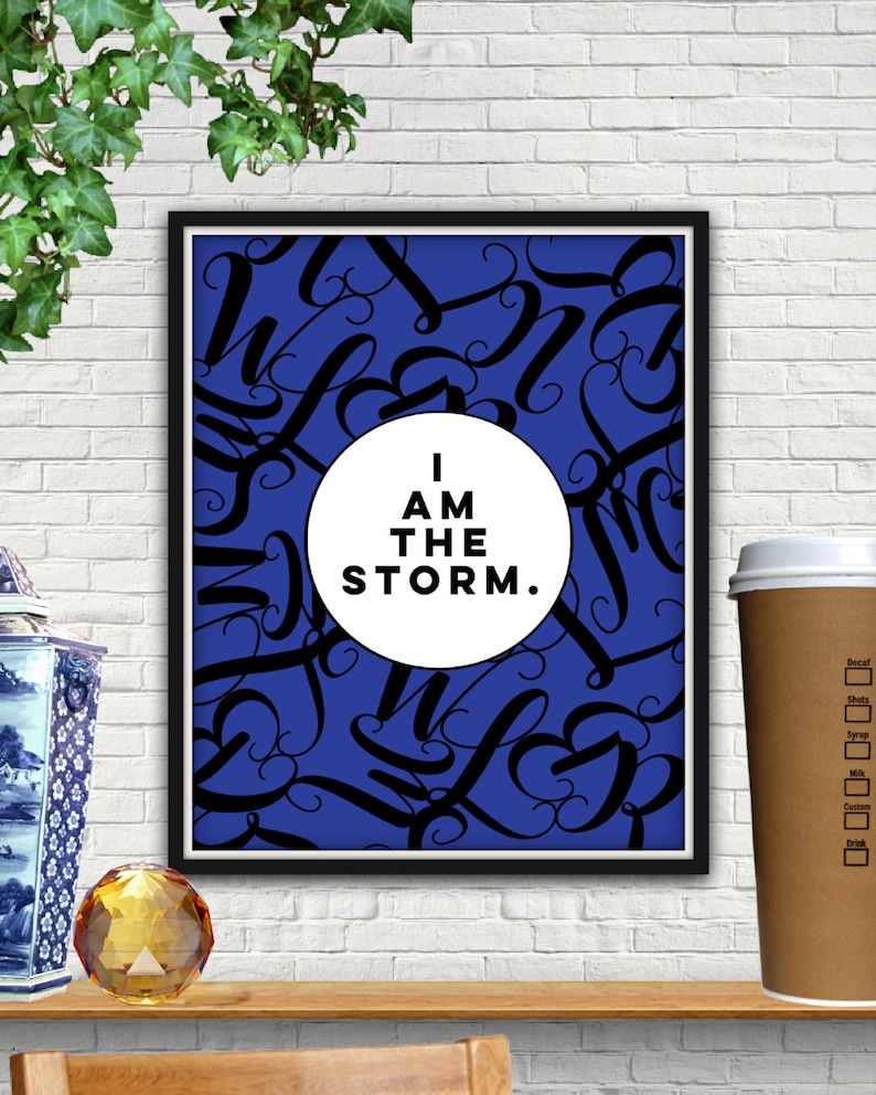 May include: A framed print with a blue background and black cursive lettering. A white circle in the center of the print contains the text "I AM THE STORM."
