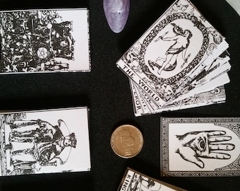 May include: A set of tarot cards with black and white illustrations. The cards are laid out on a black surface with a few crystals and a coin. The cards include "King of Pentacles", "King of Cups", and "The World".
