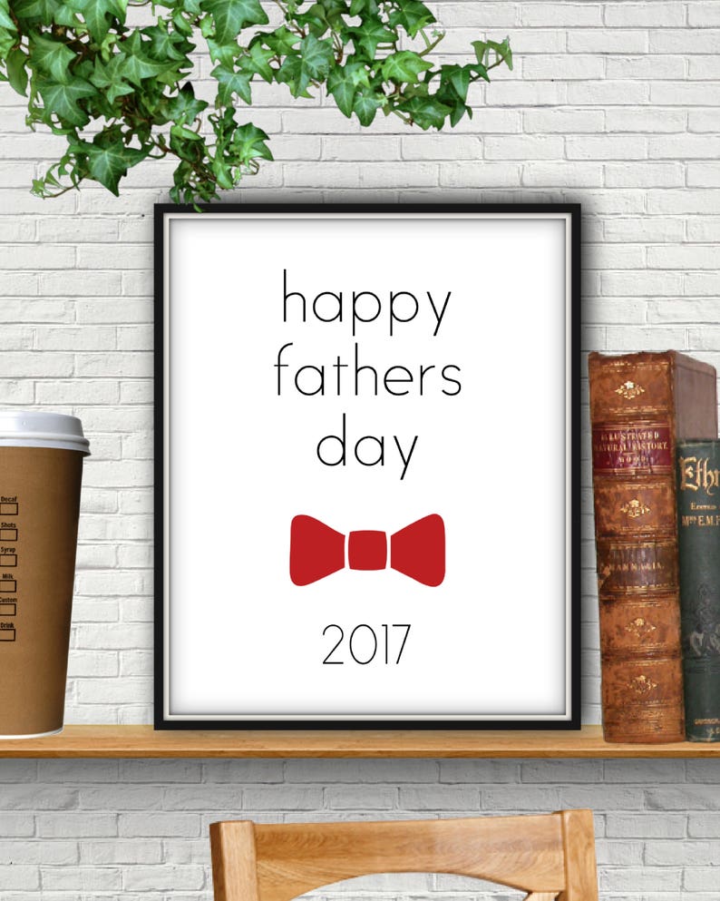 May include: A black framed print with white text that reads "happy fathers day 2017". A red bow tie is centered below the text.