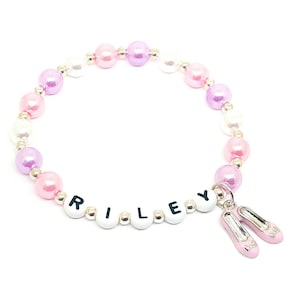May include: A pink, purple, and white beaded bracelet with the name "RILEY" spelled out in white beads and two pink ballet shoe charms.