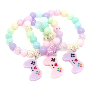 May include: Three pastel-colored beaded bracelets with a pink, purple, and light blue video game controller charm. The bracelets are made with pastel pink, light blue, lavender, and cream-colored beads.