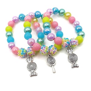 May include: Three colorful beaded bracelets with candy-shaped charms. The bracelets are made with pastel pink, blue, green, and yellow beads. The charms are silver and have a swirl design.
