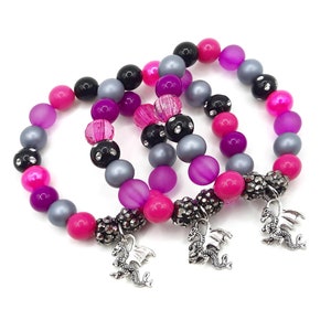 May include: Three beaded bracelets with pink, purple, black and silver beads. Each bracelet has a silver dragon charm.