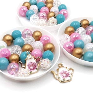 May include: Three white bowls filled with colorful beads in shades of pink, teal, gold, and white. The beads are arranged in a random pattern. Two gold teapots with floral designs are also included.