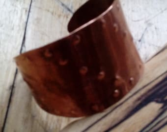 May include: A copper cuff bracelet with a hammered texture. The bracelet is a simple, yet elegant design.