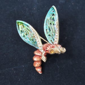 May include: A detailed insect brooch with a gold-tone body and wings. The wings are a mix of teal and green with a filigree design, accented with clear rhinestones. The insect's body is a mix of orange and brown.