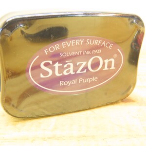 May include: A black ink pad with a label that reads "StazOn" in a purple oval with the words "For Every Surface" and "Solvent Ink Pad" above the oval and "Royal Purple" below the oval.