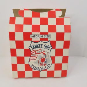 May include: A vintage "Yankee Girl Tobacco" box with a red and white chequered pattern. The box features a shield-shaped emblem with a woman holding a flag and the words "Medium Size".