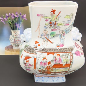May include: A white porcelain vase with a square opening and a square base. The vase is decorated with colorful hand-painted figures and landscapes. The vase has two lion-head handles.