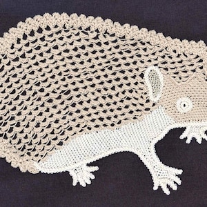 May include: A crocheted hedgehog made of beige and white yarn. The hedgehog has a detailed crocheted design with a spiky back and a small face.