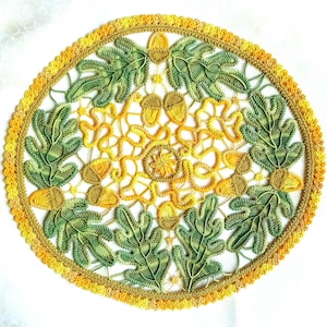 May include: A round, handmade doily featuring a detailed design of leaves and acorns. The doily is primarily yellow and green, with a scalloped edge. The intricate lace-like pattern is set against a white background.