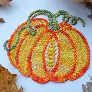 May include: A crocheted pumpkin doily in shades of orange, yellow, and green. The doily is made with a delicate lace pattern and has a raised center.