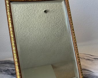 May include: Rectangular antique mirror with a decorative floral top. The frame is gold with a textured border. The flowers are yellow and peach with green leaves. The mirror is rectangular.