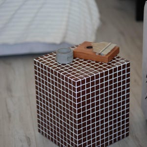 Op de afbeelding: Een kleine, vierkante, bruine betegelde bijzettafel met een houten kalimba en een grijze keramische beker erop.