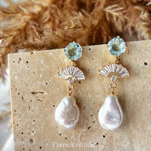 May include: Gold earrings with a light blue gemstone, a fan-shaped design with clear rhinestones, and a large white pearl drop.