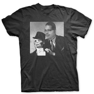 May include: A black and white photo of a man wearing a suit and tie, holding a puppet wearing a top hat and bow tie.