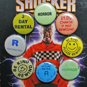 May include: A collection of eight round buttons with various colors and text. The buttons feature phrases like "3 Day Rental", "Horror", "$1.00 Charge If Not Rewound", "R Restricted", "Be Kind Please Rewind", and "This Picture Rated R".