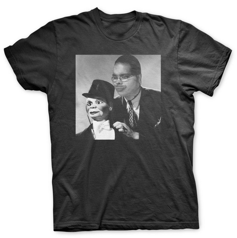 May include: A black and white photograph of a man wearing a suit and tie, holding a puppet wearing a top hat and bow tie.