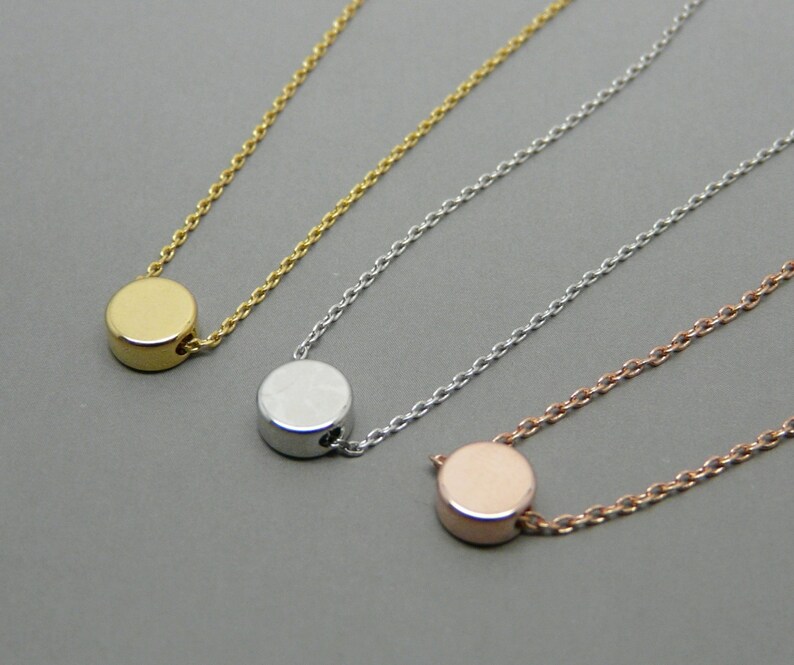 May include: Three delicate necklaces with a simple circle pendant. The necklaces are gold, silver, and rose gold.