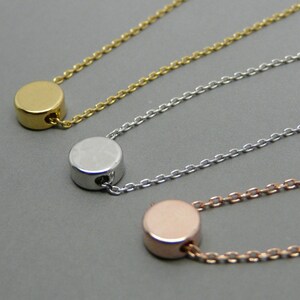 May include: Three delicate necklaces with a simple round pendant in gold, silver, and rose gold.