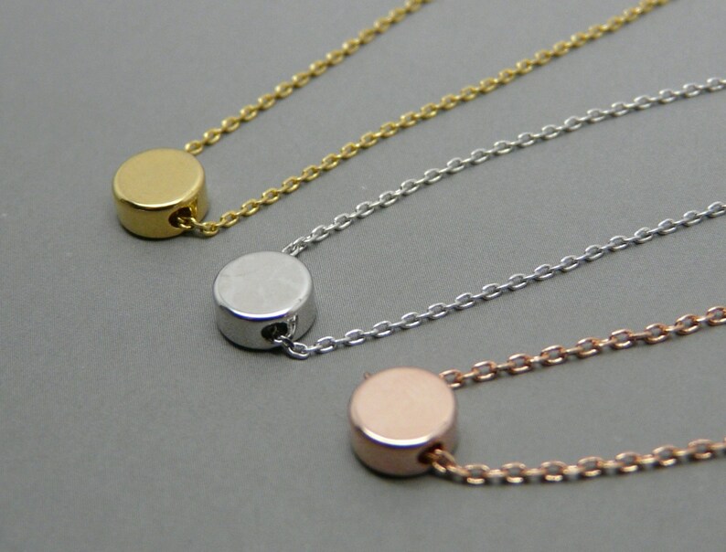 May include: Three delicate necklaces with a simple round pendant in gold, silver, and rose gold.