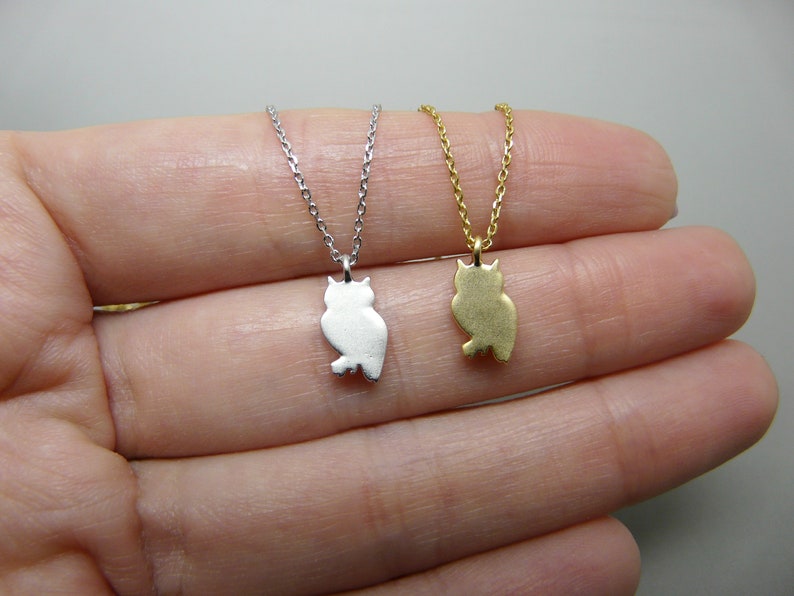 May include: Two owl pendant necklaces. One is silver-colored, the other is gold-colored. Each owl pendant is a silhouette design, hanging from a delicate chain. The necklaces are displayed against a neutral background.